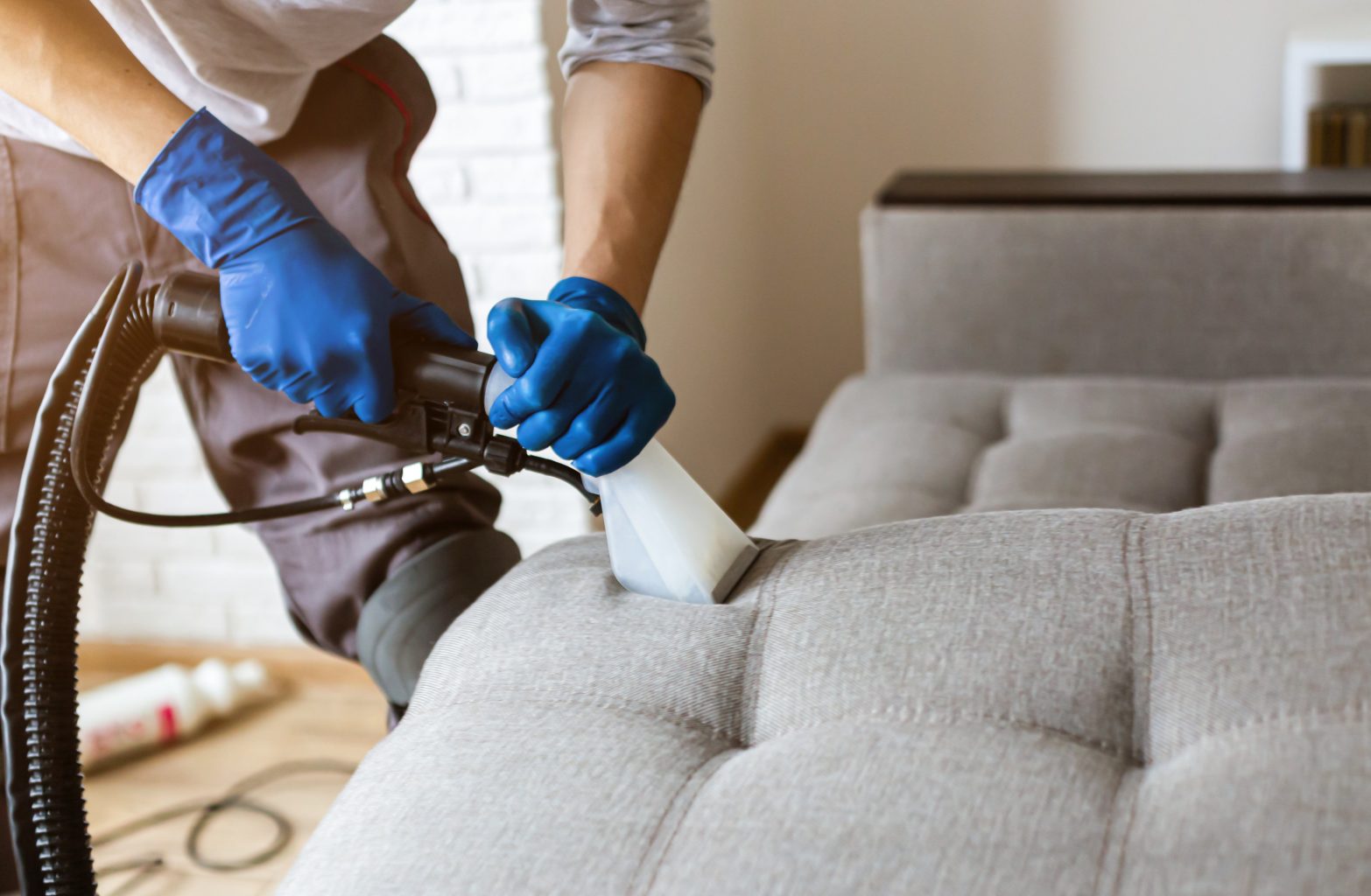 Man dry cleaner’s employee hand in protective rubber glove cleaning sofa with professionally extraction method. Early spring regular cleanup. Commercial cleaning company concept. Closeup Commercial Carpet Cleaning for Apartments in Racine, WI